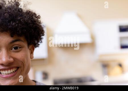 Ritratto a metà faccia di un uomo biraciale sorridente con capelli ricci in cucina a casa, copia spazio Foto Stock