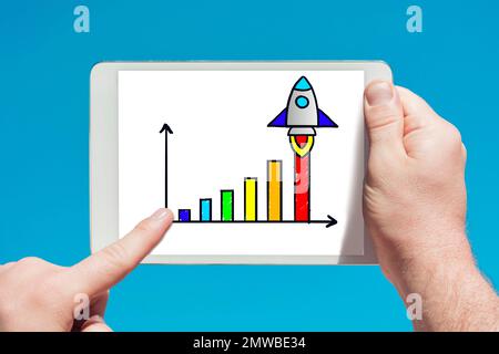 Un uomo che tiene in mano un dispositivo tablet che mostra il razzo di avvio e l'icona del grafico di crescita su sfondo blu Foto Stock