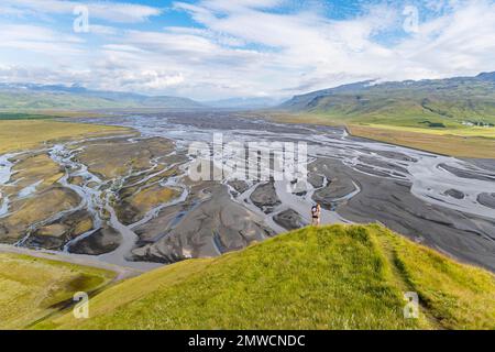 Escursionista su una collina, vista su terra alluvionale e paesaggio fluviale, meandri fluviali, Dimonarhellir, Suourland, Islanda Foto Stock