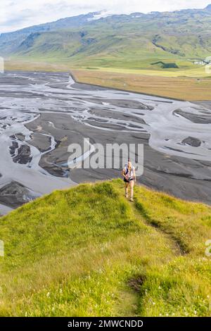 Escursionista su una collina, vista su terra alluvionale e paesaggio fluviale, meandri fluviali, Dimonarhellir, Suourland, Islanda Foto Stock