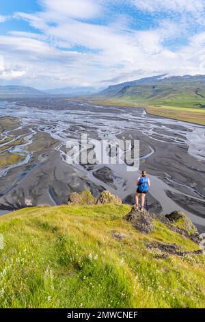 Escursionista su una collina, vista su terra alluvionale e paesaggio fluviale, meandri fluviali, Dimonarhellir, Suourland, Islanda Foto Stock