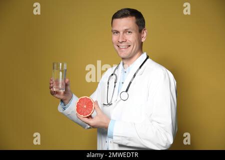 Nutrizionista che tiene un bicchiere di acqua pura e pompelmo maturo su fondo giallo Foto Stock