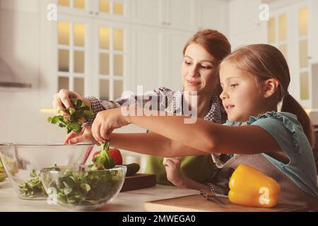 Madre e figlia cucinano l'insalata insieme in cucina Foto Stock