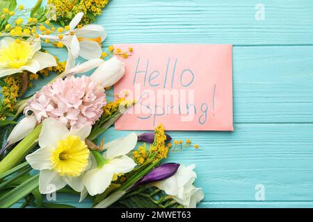 Carta rosa con parole CIAO PRIMAVERA e fiori freschi su tavolo di legno azzurro, piatto Foto Stock