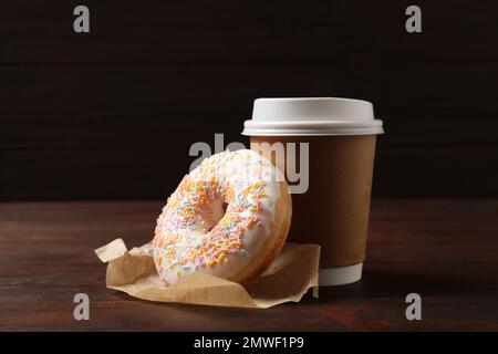 Ciambella yummy e tazza di carta su tavolo di legno su sfondo marrone Foto Stock