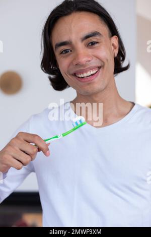 Ritratto di felice uomo biraciale spazzolando i denti in bagno Foto Stock