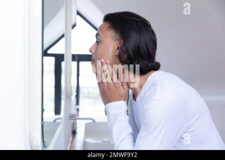 Uomo biraciale che guarda in specchio in bagno Foto Stock