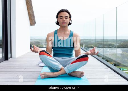 Felice uomo biraciale che fa yoga, meditando sul balcone Foto Stock