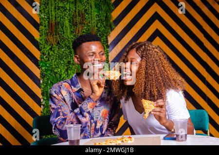 Una bella e felice coppia nera che si gusta una pizza e un drink in un bar Foto Stock