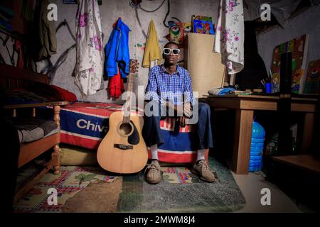 L'artista di 18 anni Anthony Blwire posa nel suo salotto durante un progetto fotografico giovani nelle loro stanze in Kibera Slum. I giovani kenioti sono spinti in una competenza di avere le proprie case lontano dai genitori, dove soprattutto imparano ad affrontare la vita attraverso diverse sfide. La competizione di avere le camere meglio decorate piene di diversi abiti di design è un modo per tenere lontano dalle sfide quotidiane della vita, come l'abuso di droghe, le gravidanze adolescenziali matrimoni precoci, e giudizi negativi da parte della gente del posto. Per la maggior parte dei giovani avere una casa è l'inizio di una nuova Foto Stock