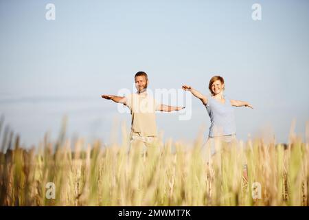 Stare spensierati e giovani a cuore. una coppia matura nella posizione del guerriero durante un workout di yoga in un campo. Foto Stock