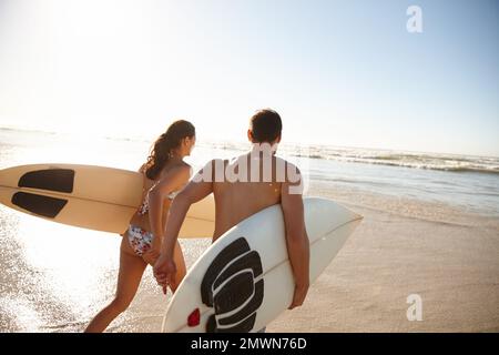 Non vedo l'ora di condividere un'onda. Ripresa da dietro di una giovane coppia di surfisti che corrono in mare insieme. Foto Stock
