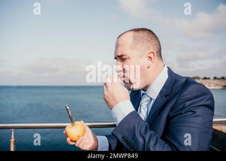 Uomo mela parco. L'uomo millenario Hippster in una cravatta e giacca prende un boccone da una mela mentre si siede su una panca del parco in slow motion Young business Foto Stock