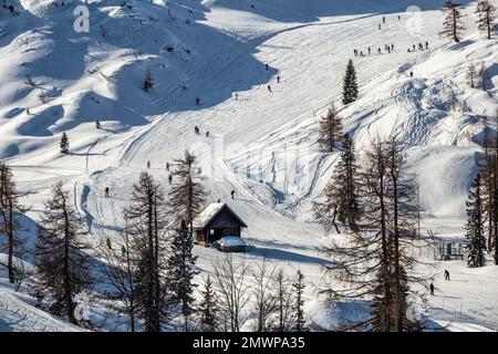 Bohinj, Slovenia - Vista invernale della montagna innevata Vogel con sciatori sulle piste da sci e capanna di legno nelle Alpi nel Parco Nazionale del Triglav su un Wi soleggiato Foto Stock