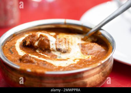 Vista ravvicinata di una ciotola di masala al burro di pollo - un cibo indiano servito su un tavolo rosso Foto Stock