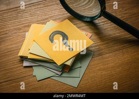 Concetto di domande e risposte. Una pila di carta con una carta in cima scritta con il simbolo della domanda insieme alle lenti d'ingrandimento. Foto Stock