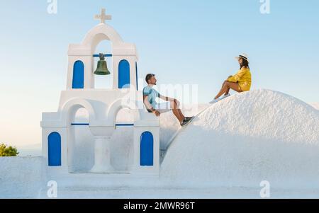 Giovani coppie di turisti uomini e donne visitano Oia Santorini Grecia in una giornata di sole durante l'estate con case e chiese imbiancate di bianco, l'isola greca Cicladi del Mar Egeo Foto Stock