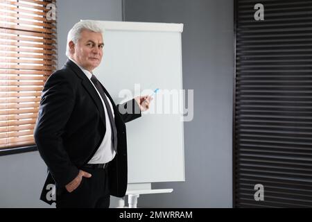 Senior Business trainer vicino alla lavagna a fogli mobili in ufficio Foto Stock