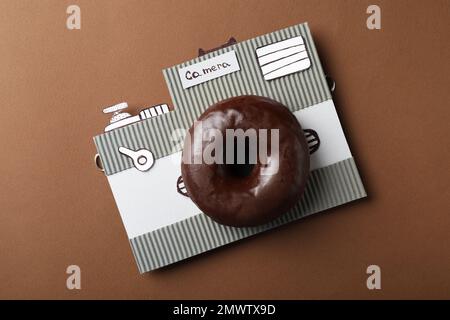 Fotocamera realizzata in ciambella e pezzo di cartone su sfondo marrone, vista dall'alto Foto Stock