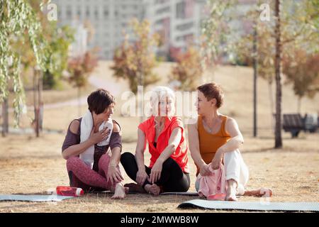 Le donne anziane attive che fanno le esercitazioni di yoga o l'addestramento di idoneità nel parco, che si distendano e che parlano dopo l'esercitazione. Felice mature amici donne all'aperto Foto Stock