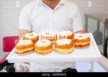 Cuoco del forno mostra la scatola delle ciambelle brioche appena fatte su un vassoio bianco Foto Stock