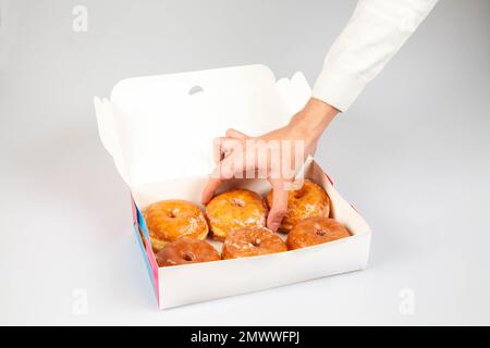 Modello per confezione di ciambelle con mano che tiene una ciambella smaltata semplice. Foto Stock