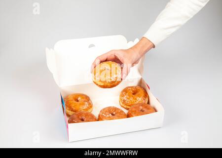 Modello per confezione di ciambelle con mano che tiene una ciambella smaltata semplice. Foto Stock