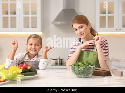 Madre e figlia cucinano l'insalata insieme in cucina Foto Stock