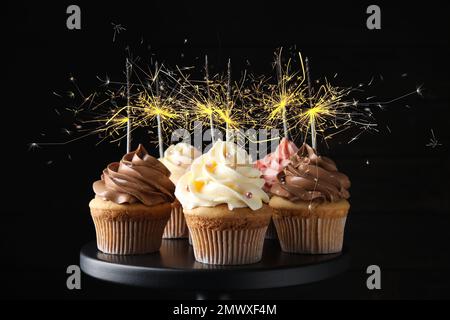 Cupcake di compleanno con scintillanti in piedi su sfondo scuro Foto Stock