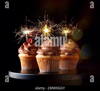 Cupcake di compleanno con scintillanti in piedi su sfondo scuro Foto Stock