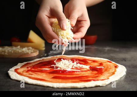 Donna che aggiunge formaggio alla pizza al tavolo grigio, primo piano Foto Stock