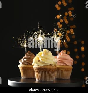 Cupcake di compleanno con scintillanti in piedi su sfondo scuro Foto Stock