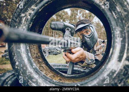 La pistola mira al bersaglio con pneumatico, paintball e uomo all'aperto, azione sul campo di battaglia e soldato fuoco durante il gioco di guerra. Sport estremo, armi e militari Foto Stock