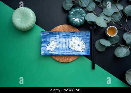 Tavolo giapponese o cinese con tradizionale tappeto da tavolo e stoviglie con sfondo verde e nero. Concetto di mangiare, mangiare, mangiare e bere. Foto Stock