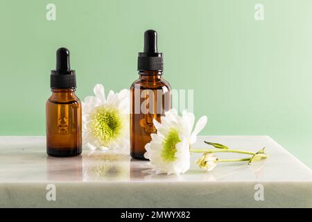 Due bottiglie cosmetiche con contagocce con siero multivitaminico idratante per il viso sono in piedi su un podio marmoreo. cura quotidiana. sfondo verde Foto Stock