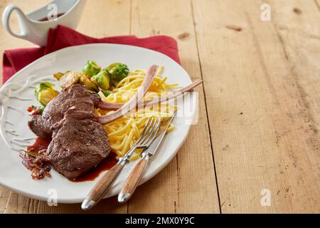 Dall'alto di deliziose bistecche alla griglia di cervo di tomahawk con spaghetti e prout di Bruxelles servite su un tavolo di legno con salsa in cucina Foto Stock