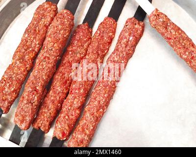 Il kebab di lula crudo sugli spiedini si trova su una piastra bianca, pronta per grigliare e chiudere Foto Stock