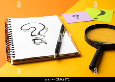 Notebook con punto interrogativo, penna e lente d'ingrandimento su sfondo colorato, primo piano Foto Stock