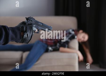 Uomo con la pistola e la sua vittima in casa, primo piano. Criminale pericoloso Foto Stock