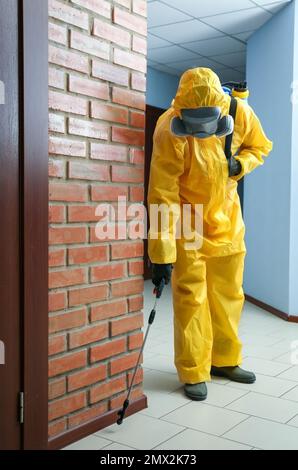 Lavoratore di controllo di peste in tuta protettiva spruzzando pesticida in interni Foto Stock