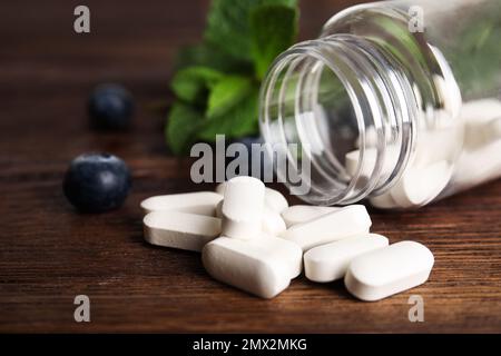 Bottiglia con pillole vitaminiche e mirtilli su tavolo di legno, primo piano Foto Stock