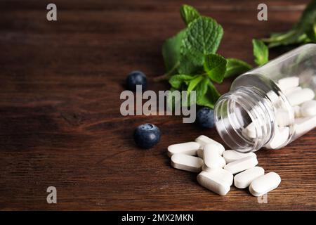 Bottiglia con pillole vitaminiche e mirtilli su un tavolo di legno. Spazio per il testo Foto Stock