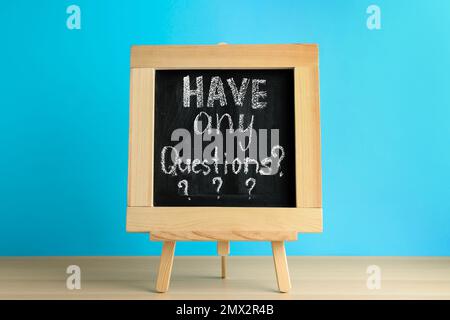 Lavagna con frase AVERE TUTTE LE DOMANDE su tavolo di legno su sfondo blu Foto Stock