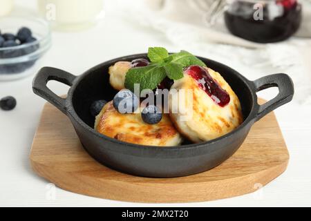 Deliziosi pancake al formaggio casolare con mirtilli, menta e marmellata in padella su un tavolo di legno bianco Foto Stock