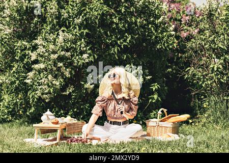 Foto di una bella bella ragazza bionda carina che tiene in mano una fragola. Attività ricreative all'aperto, picnic estivo. Foto Stock