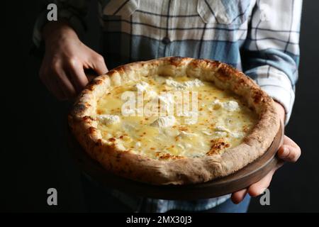 Donna che tiene deliziosa pizza al formaggio su sfondo nero, primo piano Foto Stock