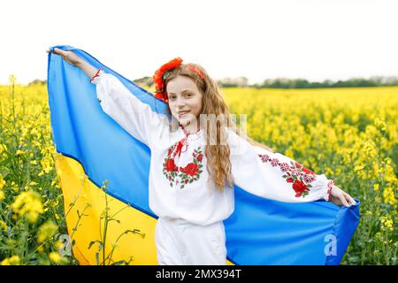 Prega per l'Ucraina. Bambino con bandiera Ucraina in campo di colza. Ragazza con bandiera nazionale in preghiera per la pace. Foto Stock