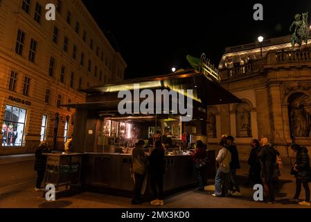 Vienna, Austria - 16 ottobre 2022: Salsiccia Bitzinger Stand, chiosco alimentare o Wurstelstand con persone in giro di notte ad Albertina, Innere Stadt, Vienna Foto Stock