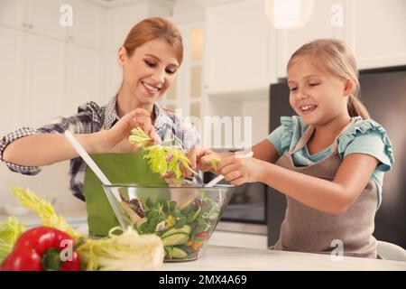 Madre e figlia cucinano l'insalata insieme in cucina Foto Stock