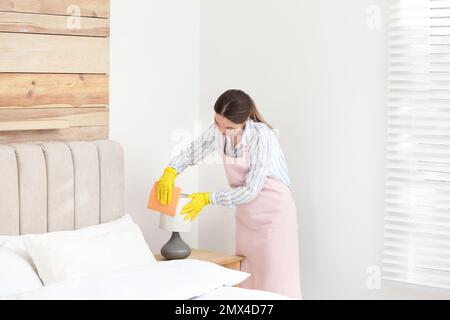 Giovane cameriera che puliva la polvere dalla lampada in camera da letto Foto Stock